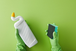 cropped view of housekeeper in rubber gloves holding sponge and bottle with toilet cleaner on green