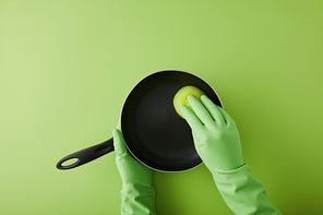 cropped view of housekeeper in rubber gloves washing frying pan with sponge on green