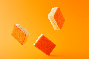 three falling sponges for dish washing on orange