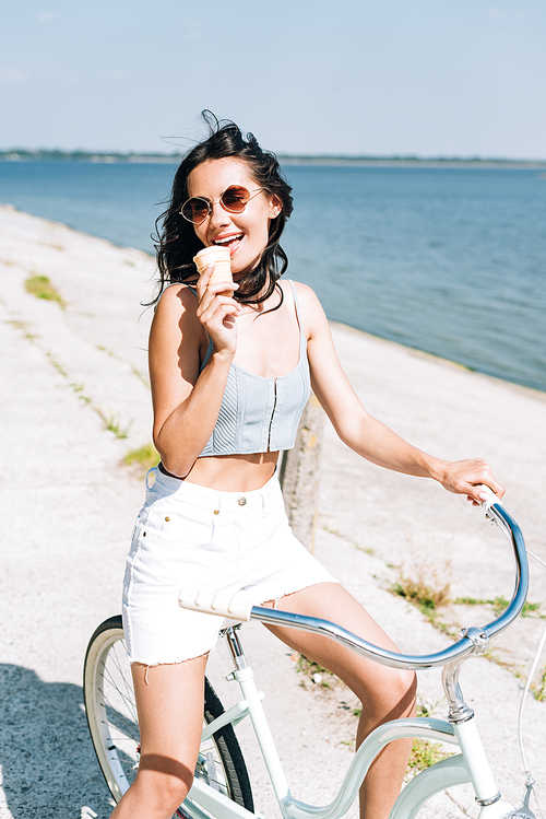 brunette girl eating ice cream and riding bike near river in summer