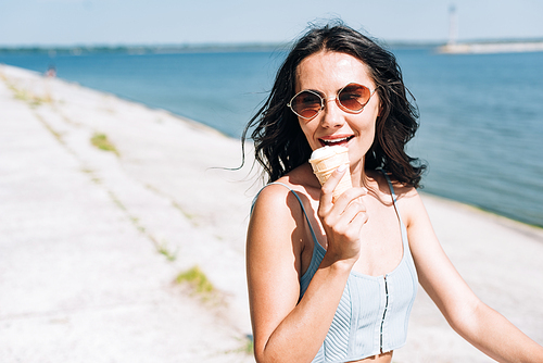 happy brunette girl eating ice cream and riding bike near river in summer
