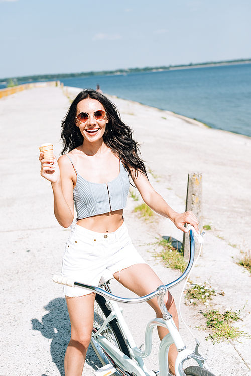 happy brunette girl with ice cream riding bike near river in summer