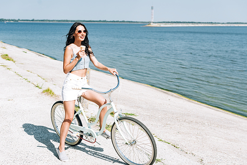 smiling brunette girl with ice cream riding bike near river in summer
