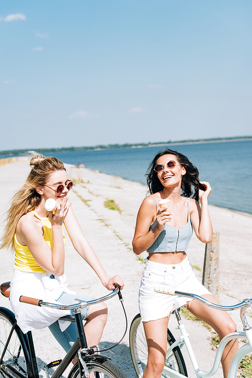 happy girls riding bikes with ice cream near river in summer