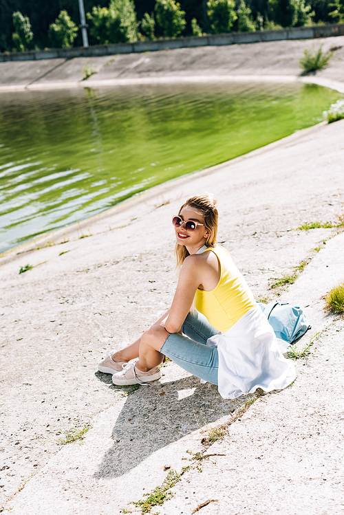 happy blonde girl sitting near river in summer