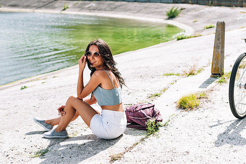 attractive brunette girl with bike sitting near river in summer