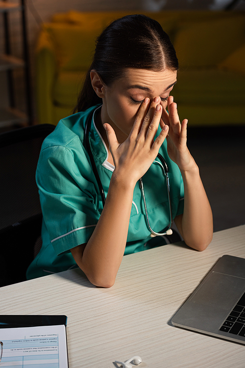 attractive and tired nurse in uniform sitting at table during night shift
