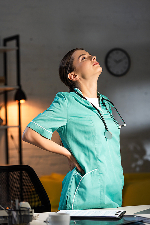 attractive nurse in uniform having back pain during night shift