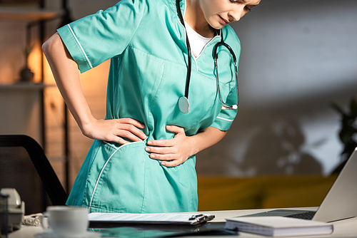 cropped view of nurse in uniform having back pain during night shift