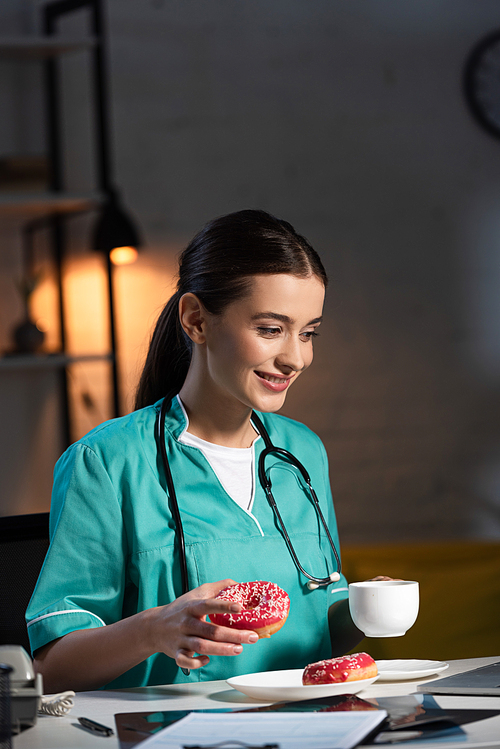 smiling nurse in uniform holding donut and cup during night shift