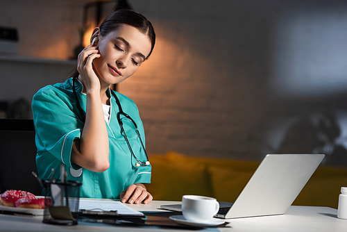 attractive nurse in uniform sitting at table and listening music during night shift