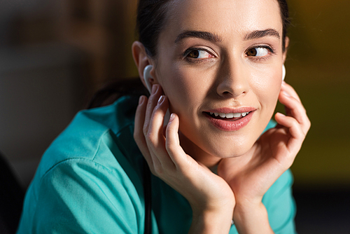 attractive and smiling nurse in uniform listening music with earphones during night shift