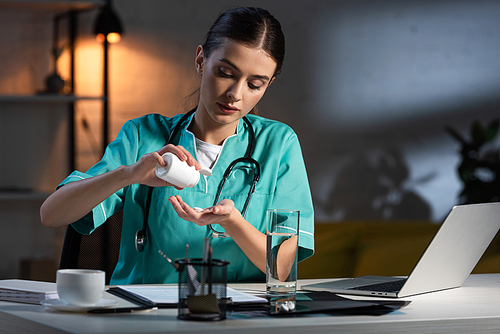 attractive nurse in uniform sitting at table and taking pill during night shift