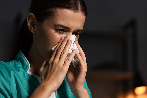 attractive nurse in uniform sneezing and holding napkin during night shift