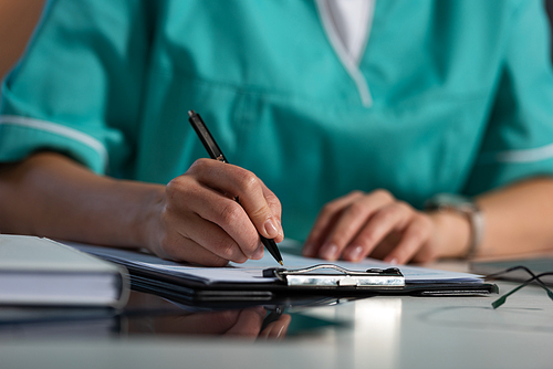 cropped view of nurse in uniform writing in clipboard during night shift