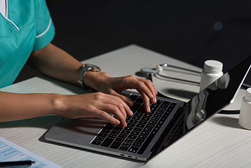 cropped view of nurse sitting at table and using laptop during night shift