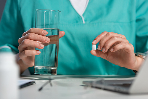 cropped view of nurse in uniform holding pill and glass of water during night shift