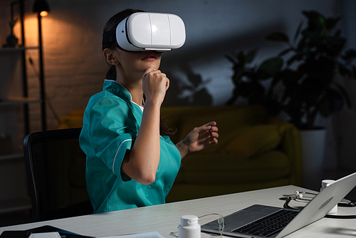 pensive nurse in uniform with virtual reality headset sitting at table during night shift