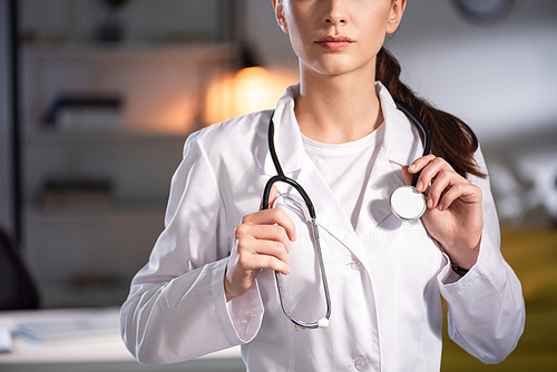 cropped view of doctor in white coat holding stethoscope during night shift