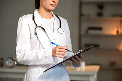 cropped view of doctor in white coat writing in clipboard during night shift