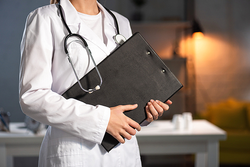 cropped view of doctor in white coat holding clipboard during night shift