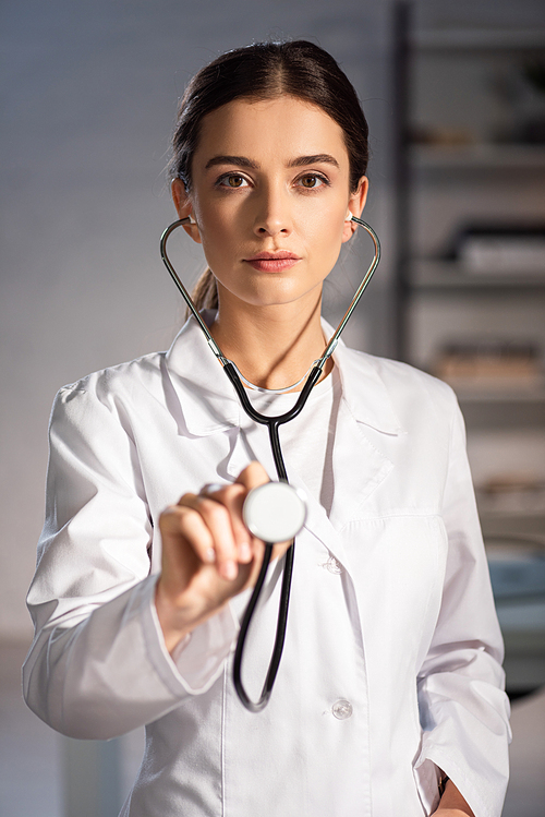 selective focus of doctor in white coat holding stethoscope during night shift