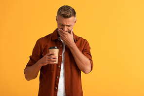 sad man covering face while looking at paper cup isolated on orange