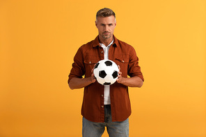 serious man holding football isolated on orange