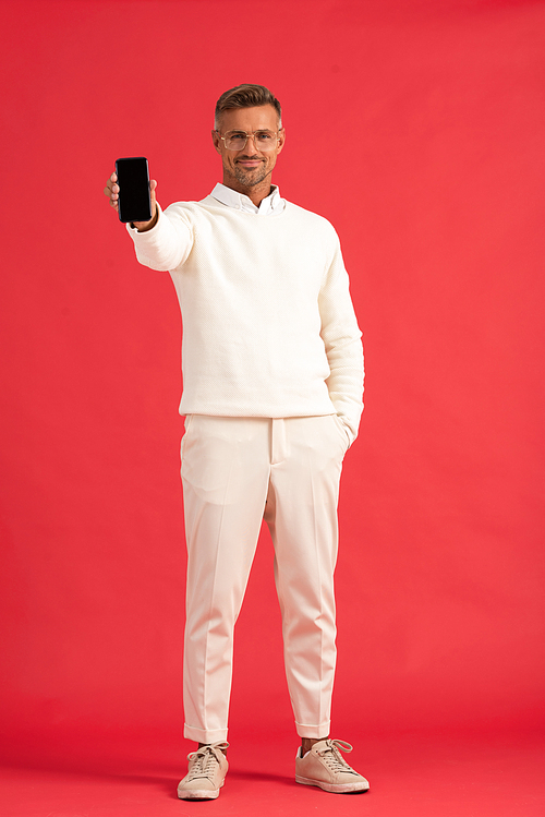 happy man holding smartphone with blank screen while standing with hand in pocket