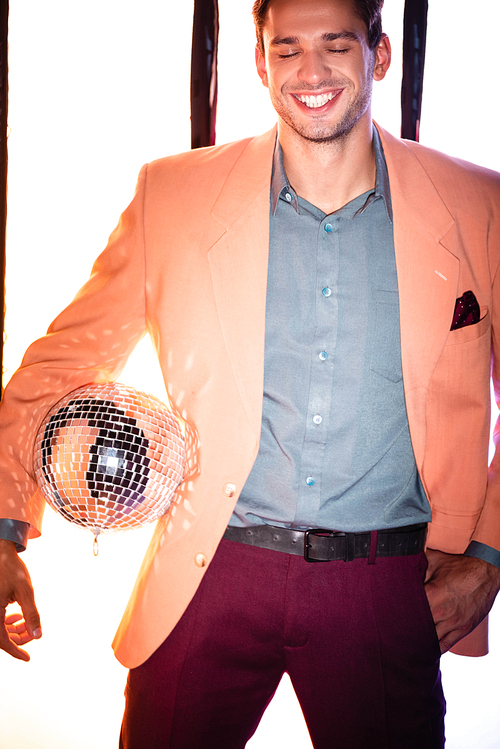 happy man in blazer standing with with hand in pocket and holding disco ball on white with black stripes
