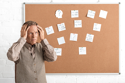 retired man with alzheimer disease touching head and standing near board with papers and letters