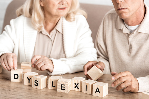 cropped view of senior woman sitting near sick husband and wooden cubes with dyslexia letters