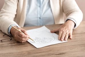 cropped view of retired woman holding paper with drawing on table