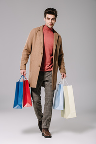 stylish man in beige coat holding shopping bags on grey