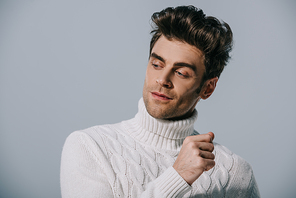 handsome fashionable man posing in white knitted sweater, isolated on grey