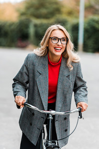 attractive businesswoman in coat and glasses smiling and riding bike