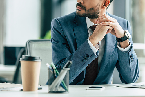 cropped view of businessman sitting at workplace with folded hands