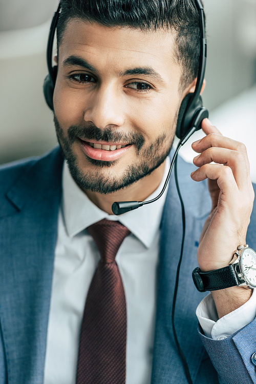 handsome call center operator touching headset while working in office