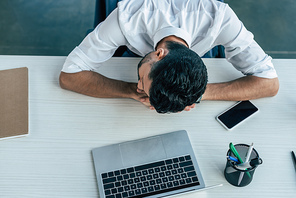 top view of exhausted businessman sleeping at workplace near laptop and smartphone