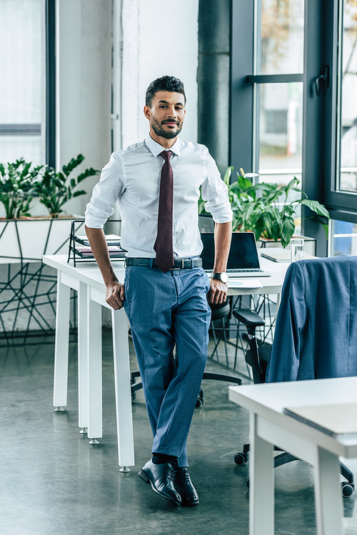 young confident businessman standing near desk and 