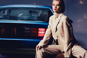 attractive and stylish woman sitting near retro car and looking at camera