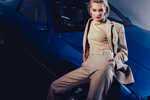 attractive and stylish woman in suit sitting on retro car