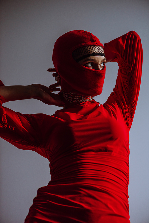 stylish woman in red dress and balaclava isolated on grey