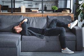 side view of handsome man with headache lying on sofa in apartment