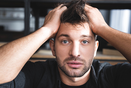 handsome man with panic attack touching head in apartment