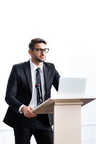 businessman in suit standing at podium tribune and looking away during conference isolated on white
