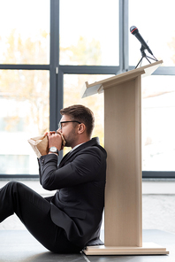 side view of scared businessman in suit breathing in paper bag during conference