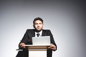 low angle view of scared businessman in suit standing at podium tribune and looking away during conference on white background