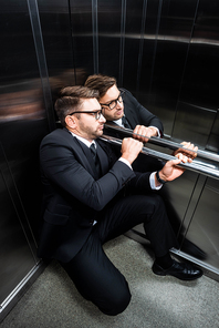 high angle view of scared businessman in suit with claustrophobia sitting on floor in elevator