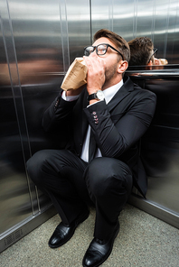 scared businessman in suit with claustrophobia breathing in paper bag in elevator
